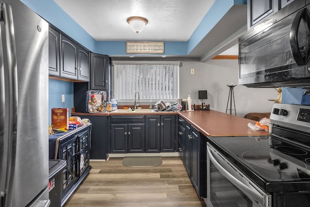 kitchen with a textured ceiling, stainless steel appliances, light wood-type flooring, and a sink