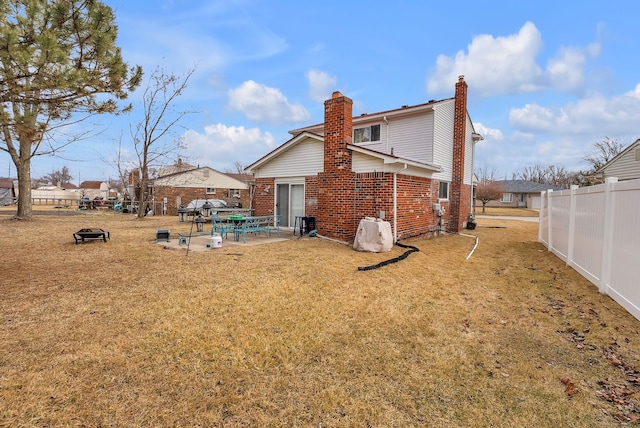 rear view of property featuring a patio, fence, a chimney, a lawn, and brick siding