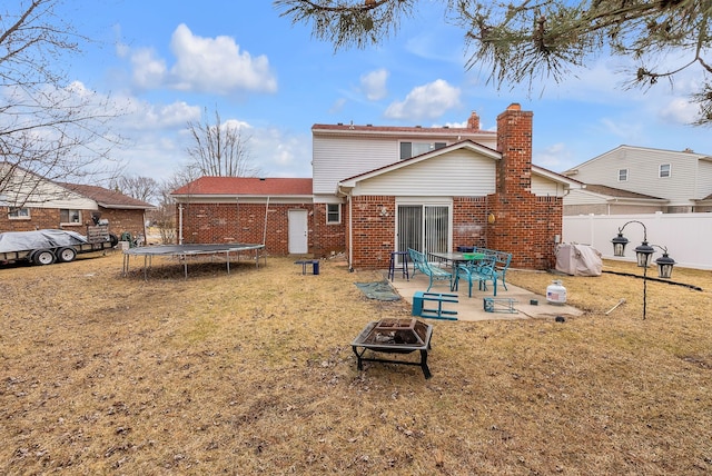 back of house with a trampoline, fence, a fire pit, brick siding, and a patio area