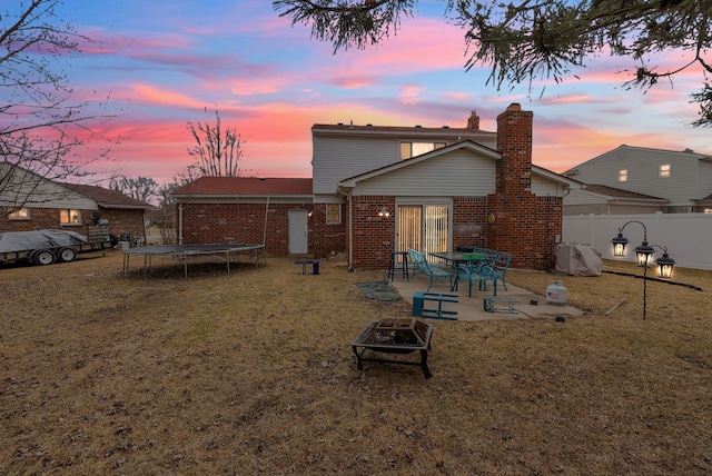 back of house with a trampoline, an outdoor fire pit, fence, a yard, and a patio area