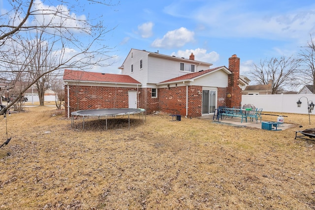 back of house featuring brick siding, a trampoline, fence, a chimney, and a patio area