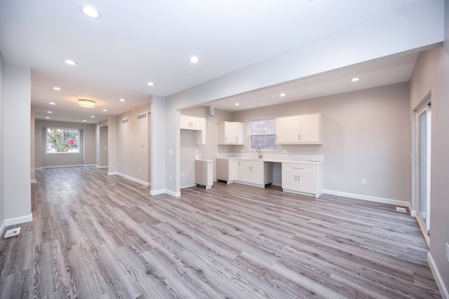 unfurnished living room featuring sink, built in desk, and light hardwood / wood-style floors