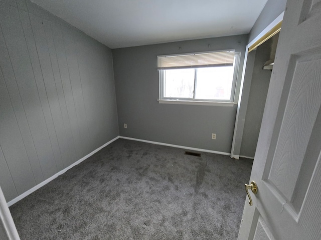 unfurnished bedroom with dark carpet and wooden walls