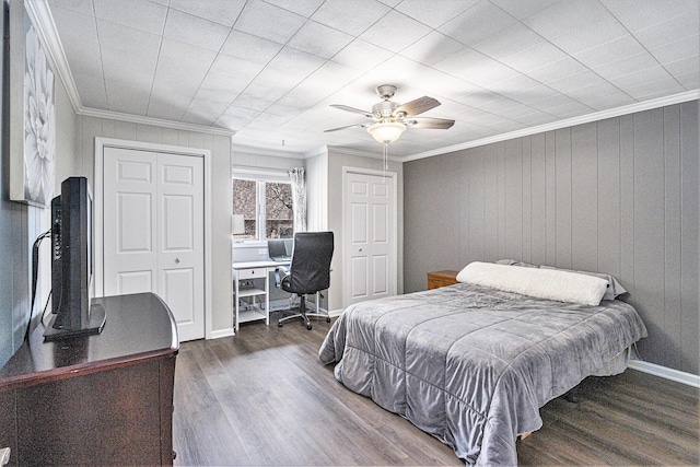 bedroom with crown molding, dark wood-type flooring, two closets, and ceiling fan