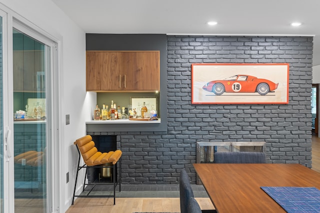 interior space with indoor bar, brick wall, and light hardwood / wood-style flooring