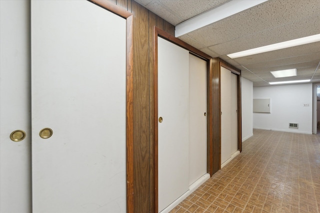 hallway with baseboards, visible vents, and a drop ceiling