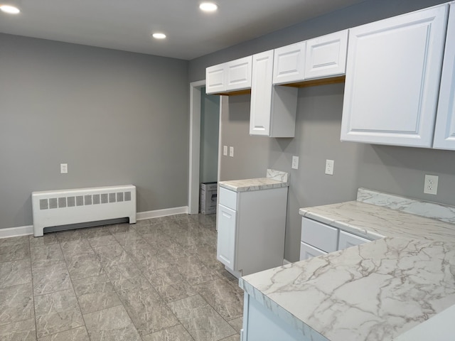 kitchen with light stone countertops, radiator, and white cabinets