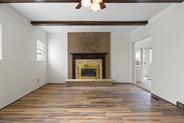 unfurnished living room featuring hardwood / wood-style flooring, a wealth of natural light, a fireplace, and beam ceiling