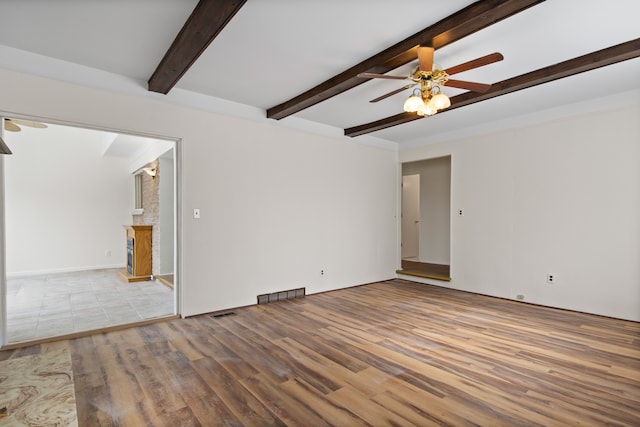 spare room featuring beamed ceiling, ceiling fan, a brick fireplace, and light hardwood / wood-style flooring