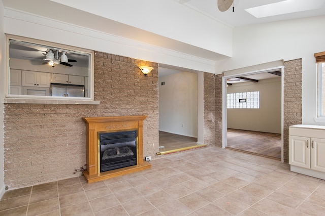 unfurnished living room with vaulted ceiling with skylight, brick wall, light tile patterned floors, and ceiling fan