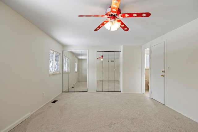 unfurnished bedroom with light colored carpet and two closets