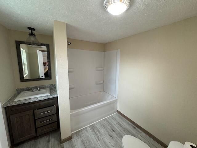 full bathroom featuring hardwood / wood-style flooring, washtub / shower combination, vanity, a textured ceiling, and toilet