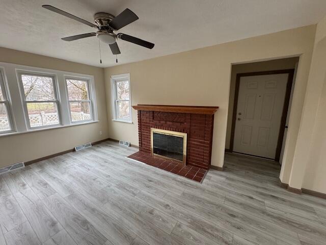 unfurnished living room featuring a brick fireplace, ceiling fan, and light wood-type flooring