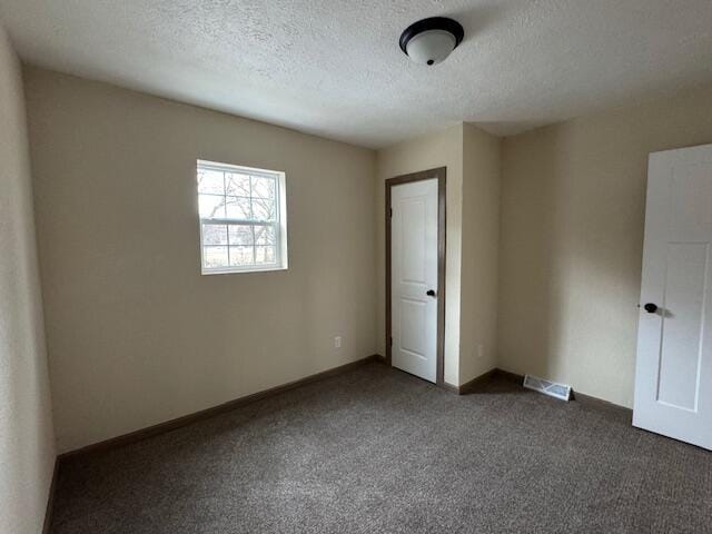 unfurnished bedroom featuring a textured ceiling and dark colored carpet