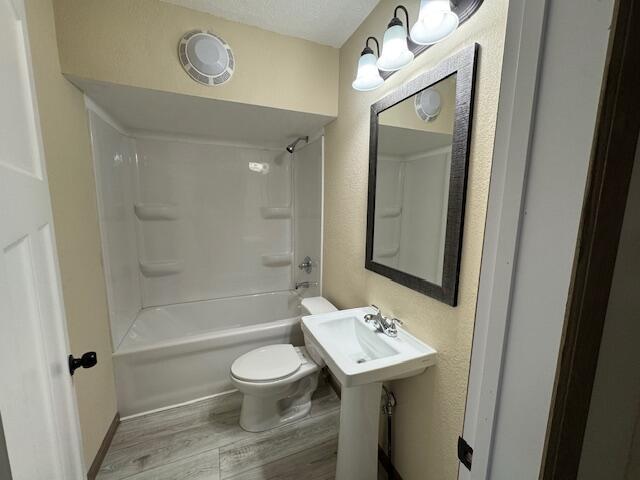 full bathroom featuring toilet, sink, wood-type flooring, a textured ceiling, and shower / washtub combination