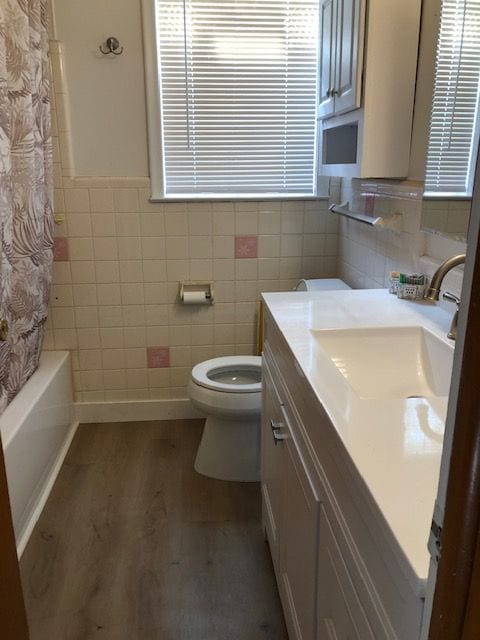 full bathroom featuring hardwood / wood-style flooring, shower / tub combo, toilet, tile walls, and vanity