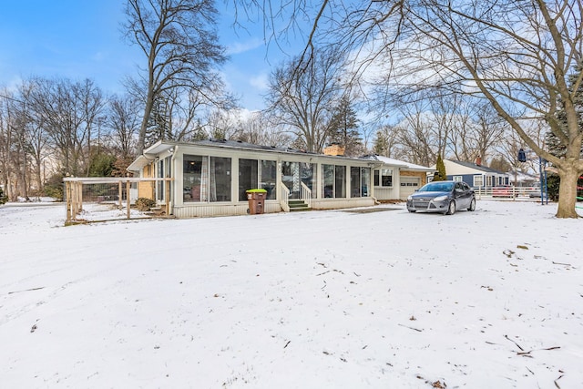 snow covered rear of property with a sunroom