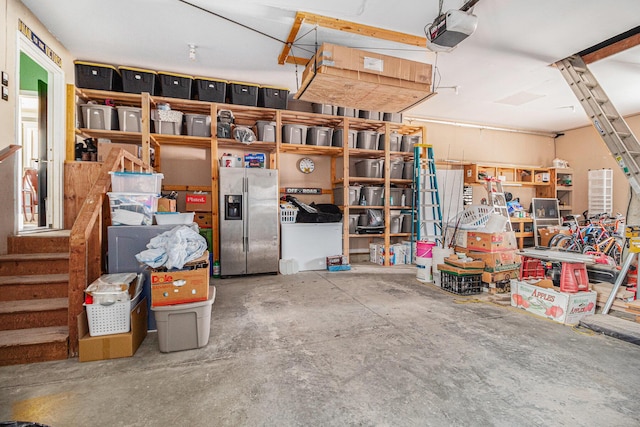 garage with stainless steel refrigerator with ice dispenser and a garage door opener