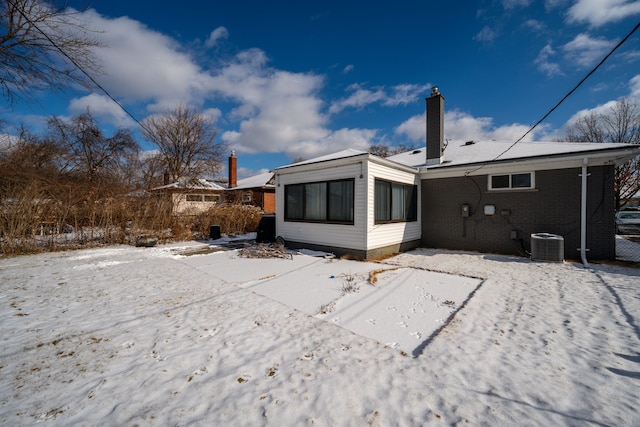 snow covered rear of property featuring central AC