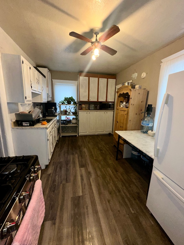 kitchen featuring stainless steel gas stove, a textured ceiling, white refrigerator, dark hardwood / wood-style floors, and white cabinets