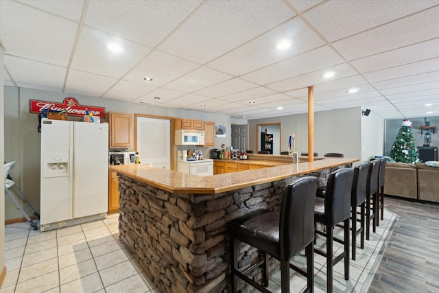 kitchen with a drop ceiling, light brown cabinets, white appliances, a kitchen breakfast bar, and open floor plan