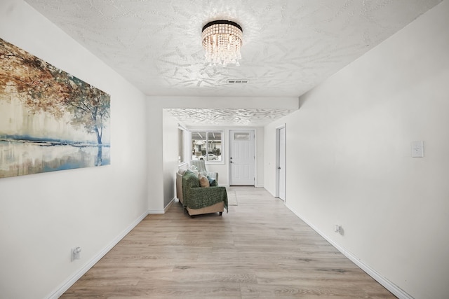 hallway featuring an inviting chandelier, light hardwood / wood-style floors, and a textured ceiling