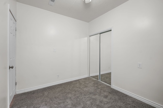 unfurnished bedroom with dark carpet, a closet, and a textured ceiling