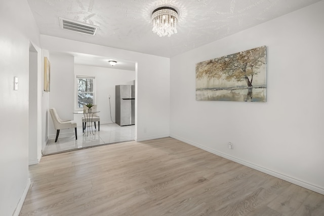 spare room with a chandelier, a textured ceiling, and light wood-type flooring