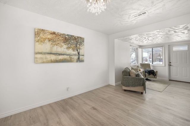 unfurnished room featuring a notable chandelier, a textured ceiling, and light wood-type flooring