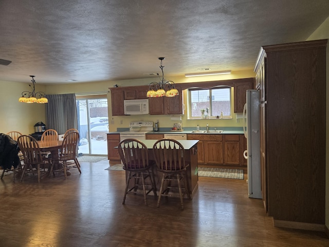 kitchen featuring sink, white appliances, dark hardwood / wood-style floors, a kitchen island, and decorative light fixtures