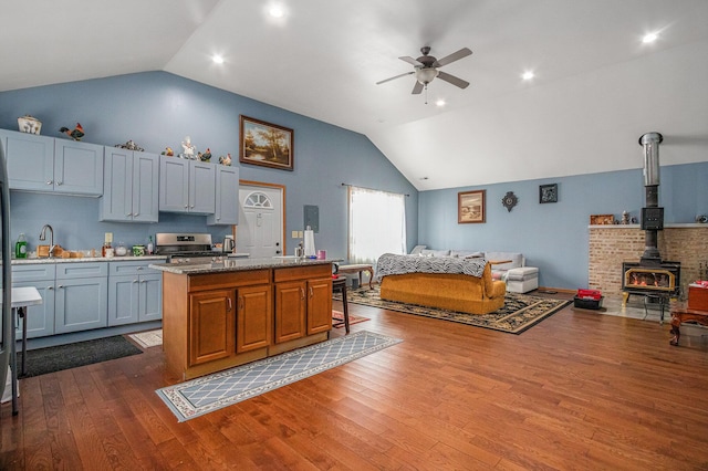 kitchen featuring light stone counters, wood-type flooring, an island with sink, and a wood stove