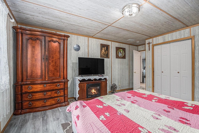 bedroom featuring hardwood / wood-style flooring, ornamental molding, wood ceiling, and a closet