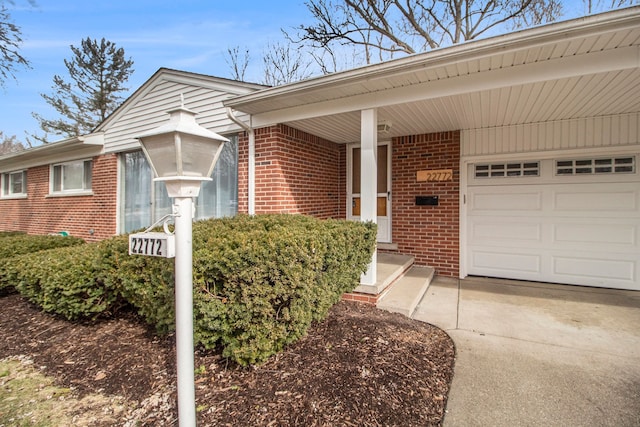 doorway to property with an attached garage, driveway, and brick siding