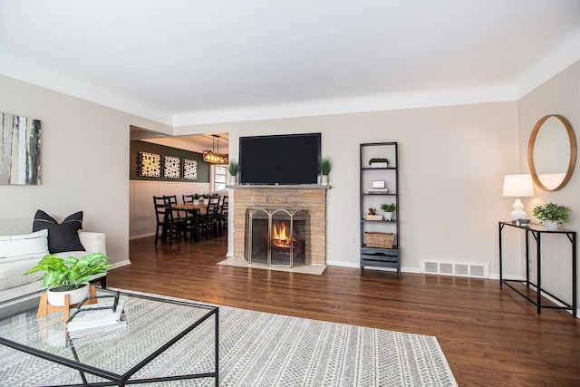 living area with a stone fireplace, wood finished floors, visible vents, and baseboards