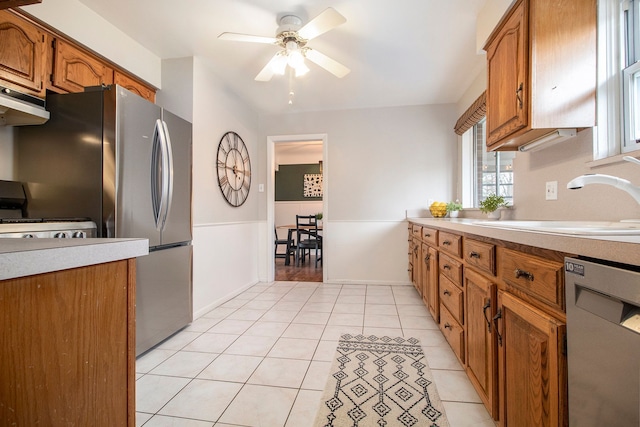 kitchen with light tile patterned flooring, under cabinet range hood, a sink, appliances with stainless steel finishes, and brown cabinets