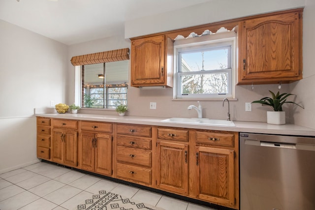 kitchen with light tile patterned floors, dishwasher, brown cabinets, light countertops, and a sink