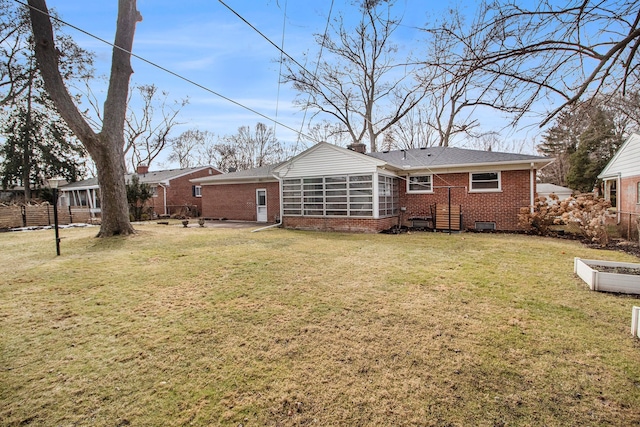 rear view of house featuring brick siding, a chimney, a lawn, a sunroom, and fence