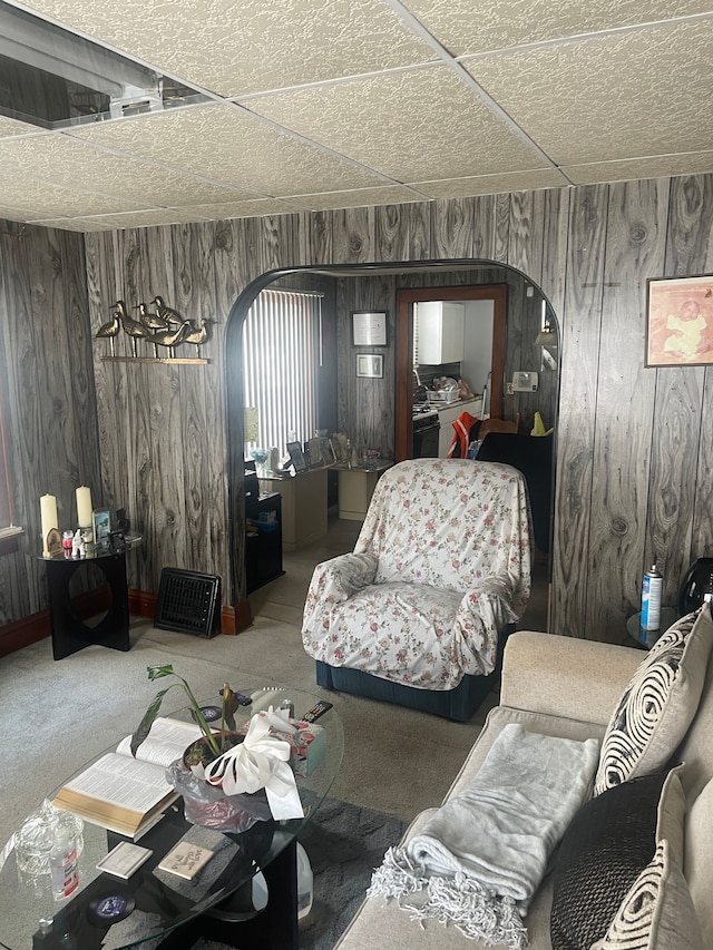 living room featuring carpet floors, a paneled ceiling, and wooden walls