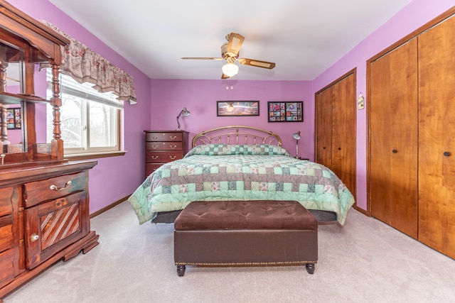 bedroom with ceiling fan, light colored carpet, and two closets