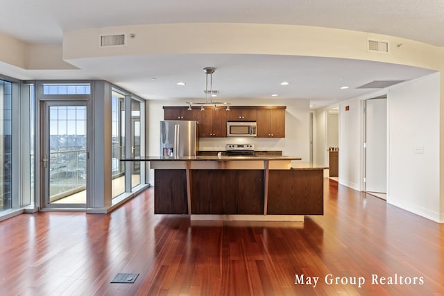 kitchen with pendant lighting, appliances with stainless steel finishes, dark hardwood / wood-style floors, expansive windows, and a center island with sink