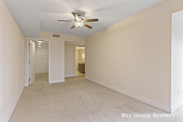 unfurnished bedroom with light carpet, a spacious closet, a closet, and ceiling fan