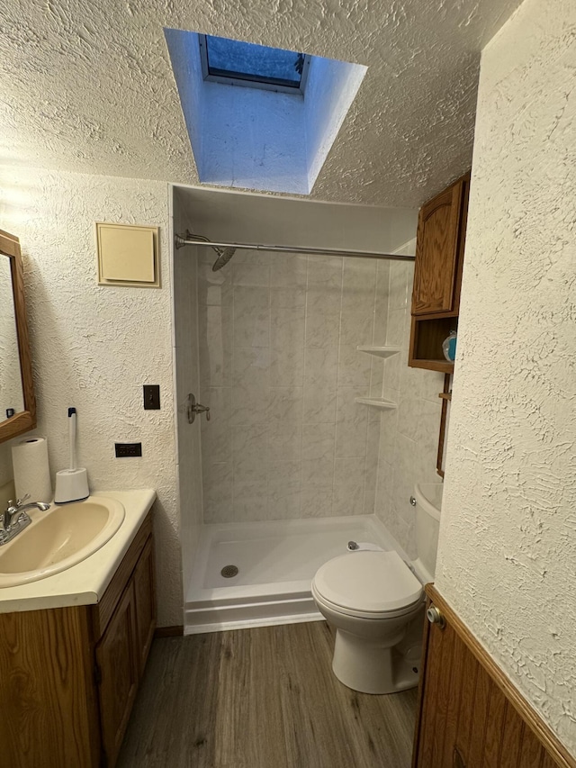 bathroom with toilet, wood-type flooring, a textured ceiling, a tile shower, and vanity