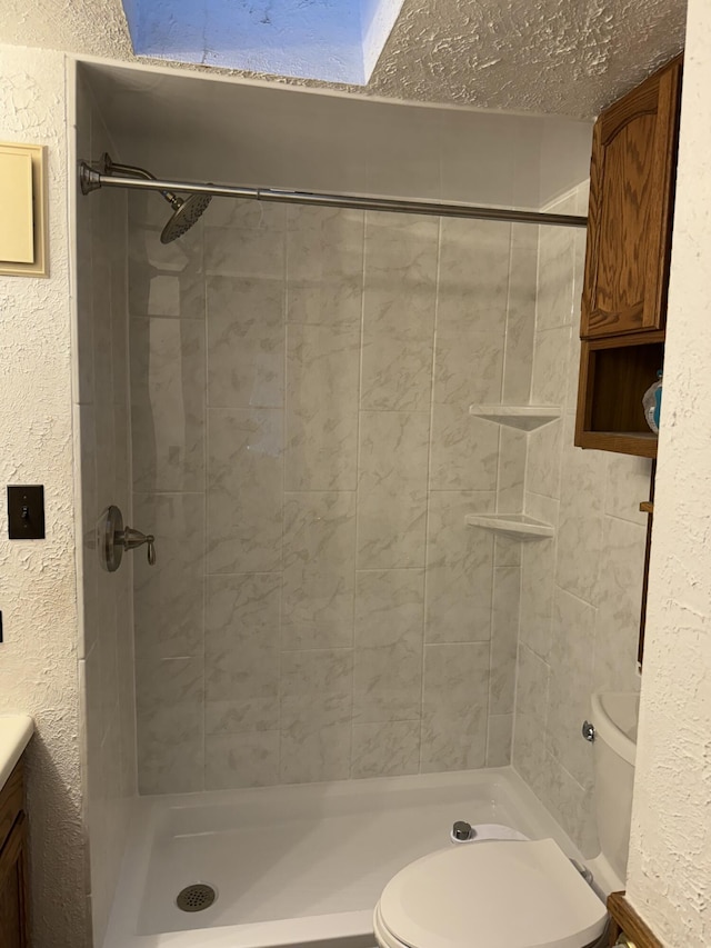 bathroom featuring vanity, a tile shower, a textured ceiling, and toilet