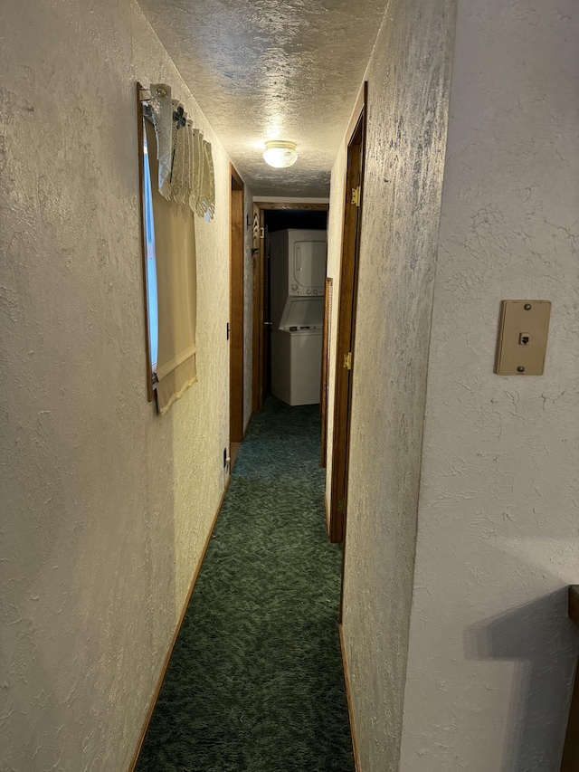 hallway with stacked washing maching and dryer, dark carpet, and a textured ceiling