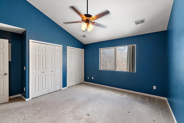 unfurnished bedroom with two closets, vaulted ceiling, light colored carpet, and ceiling fan