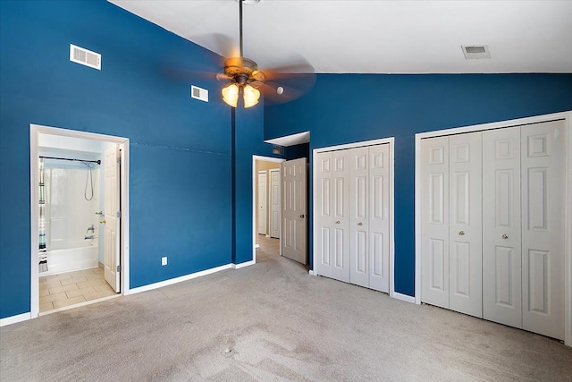 unfurnished bedroom with ceiling fan, high vaulted ceiling, connected bathroom, light carpet, and two closets