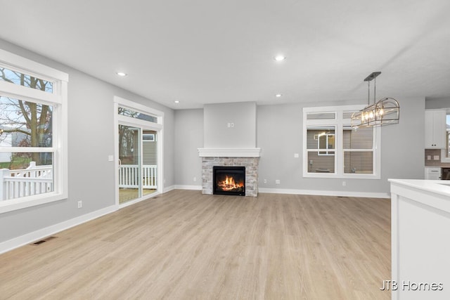 unfurnished living room with light wood-type flooring, a chandelier, and a stone fireplace