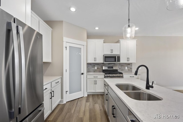 kitchen featuring appliances with stainless steel finishes, white cabinetry, sink, hanging light fixtures, and light stone counters