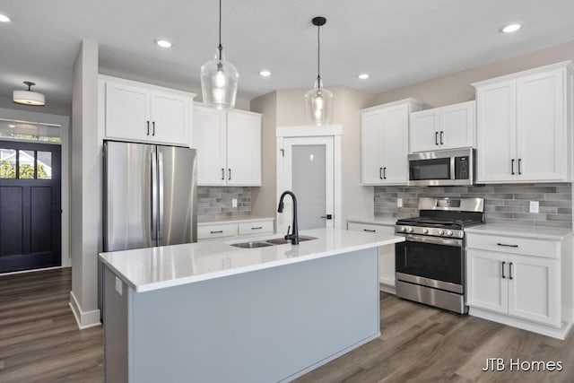 kitchen featuring sink, hanging light fixtures, stainless steel appliances, an island with sink, and white cabinets