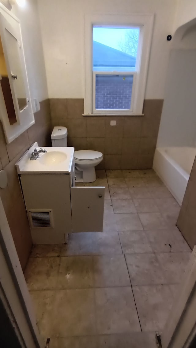 bathroom featuring tile patterned floors, toilet, tile walls, vanity, and a bathing tub